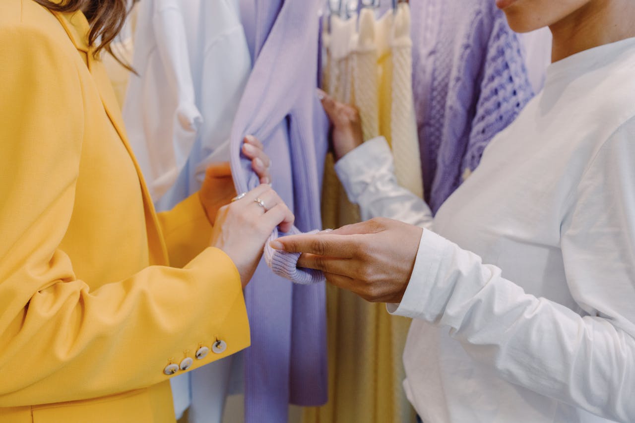 Services Two women examining vibrant clothing on a rack inside a boutique.